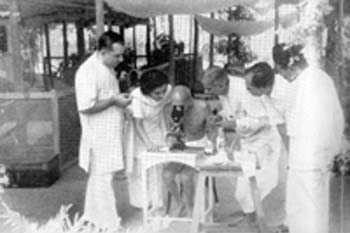 Gandhiji inspecting the 'hook worms' through microscope during his convalesce at Jehangir Patel's hut in Juhu, Bombay. May 1944